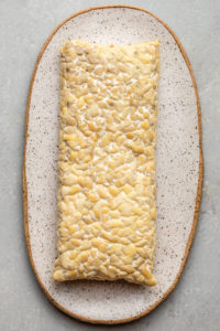 block of uncut tempeh on white serving board