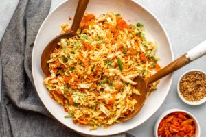 cooked ramen noodle salad with kimchi in large white bowl with wooden serving spoons
