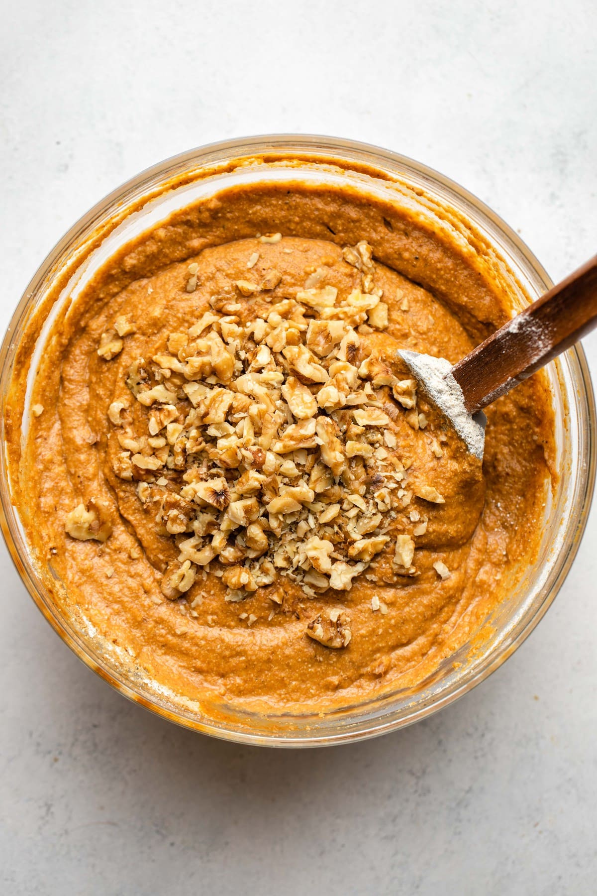 pumpkin muffin batter in glass bowl with walnuts sprinkled on top