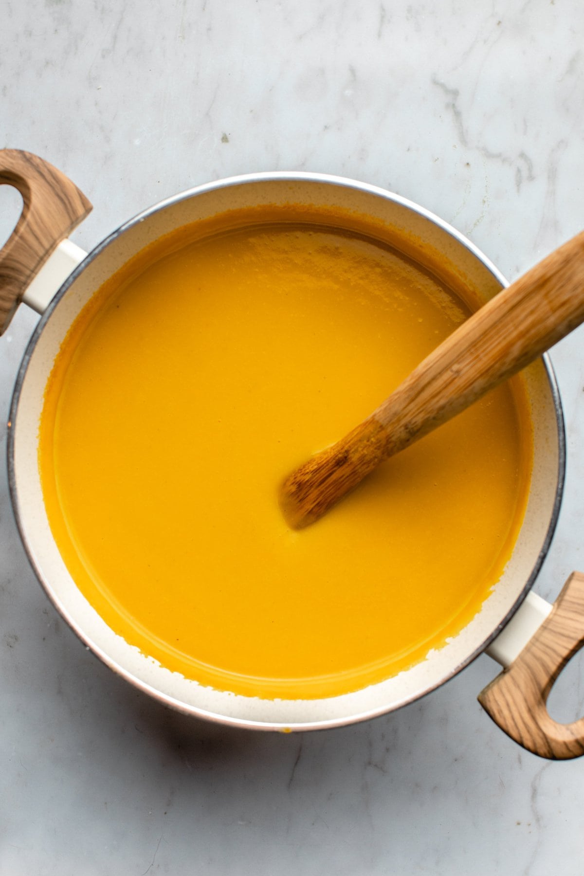 blended butternut squash soup in white pot with wooden spoon