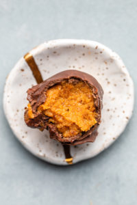chocolate covered pumpkin truffle on small white plate with bite taken out of it