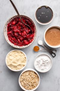 ingredients for cranberry orange crumble bars in small white bowls on marble background