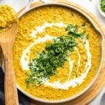 pot of red lentil curry topped with coconut milk and cilantro on white background