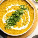 large white pot of red lentil curry topped with coconut milk and cilantro