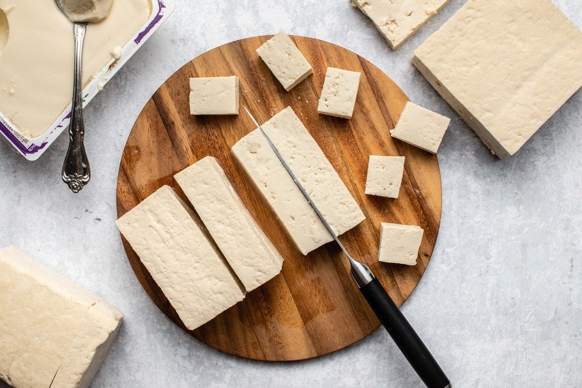 cubed and sliced tofu on round wooden cutting board on marble background