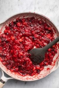 cooked cranberry sauce in grey saucepan with dark grey rubber spatula