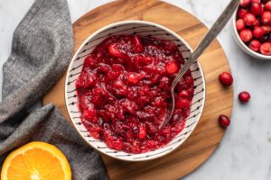 healthy cranberry sauce in white bowl with spoon on wood cutting board and marble background