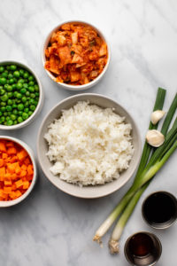 ingredients for kimchi fried rice in small bowls on marble background