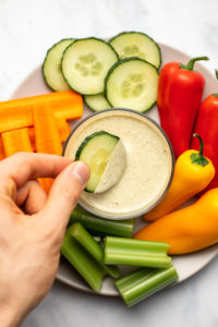 hand dunking slice of cucumber into vegan ranch dressing