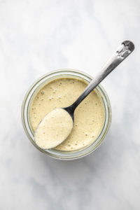glass jar of vegan ranch dressing with silver spoon on white background