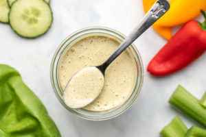 glass jar of vegan ranch dressing surrounded by colorful vegetables