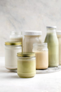 homemade nut milks in different sized glass jars on white background