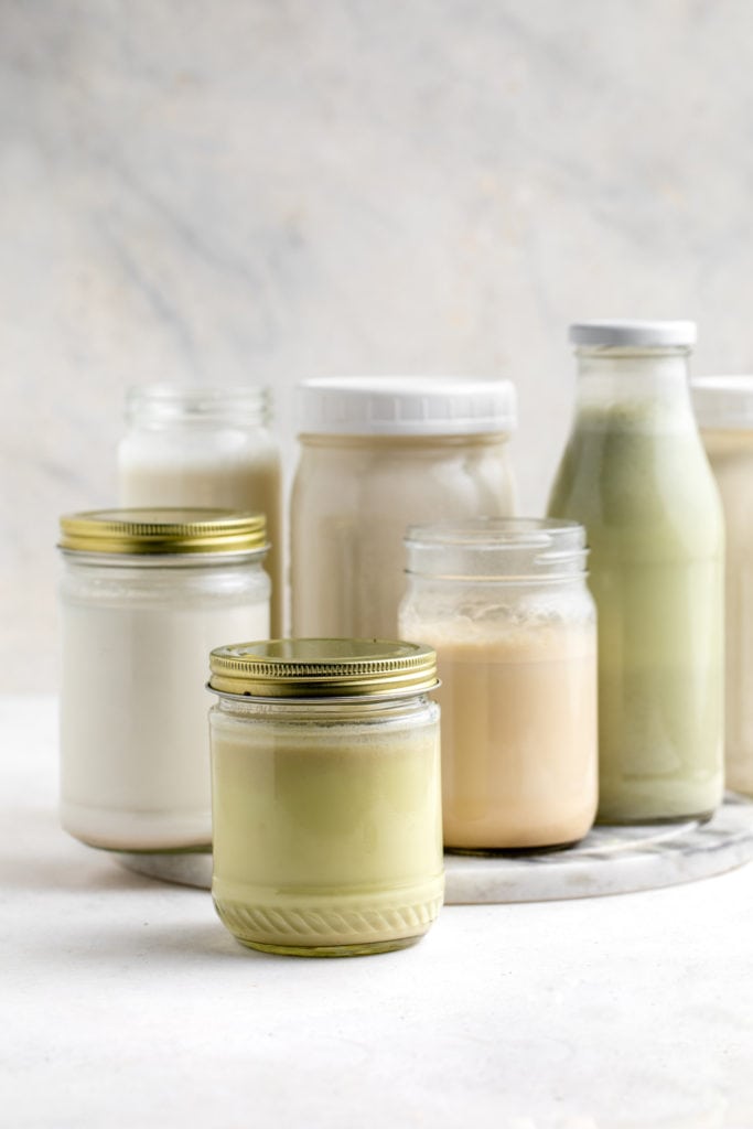 homemade nut milks in different sized glass jars on white background