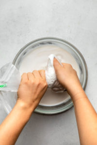 hands twisting nut milk bag and straining into large glass bowl