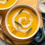 white bowl of butternut squash and apple soup with coconut milk swirl on wooden cutting board