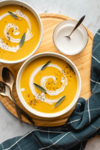 two bowls of butternut squash and apple soup in white bowl on wooden cutting board with marble background