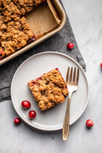 cranberry orange crumble bar on small grey plate decorated with fresh cranberries and a small fork