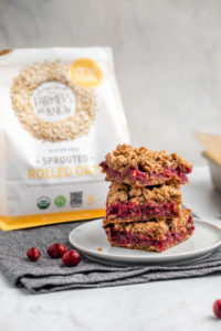 stack of cranberry orange bars on small grey plate with bag of one degree organics sprouted rolled outs in background