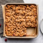 cranberry orange crumble bars in gold pan with parchment paper on marble background