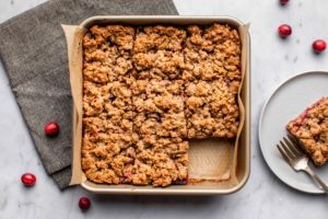 cranberry orange crumble bars in gold pan with parchment paper on marble background