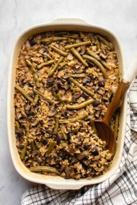 green bean and wild rice casserole in large casserole dish with wooden spoon on marble background