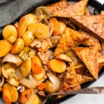 slow cooker tempeh pot roast with golden tempeh and cooked vegetables on black serving tray on grey background