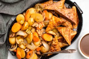 slow cooker tempeh pot roast with golden tempeh and cooked vegetables on black serving tray on grey background
