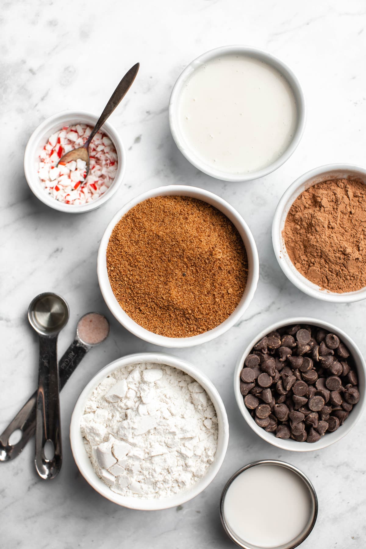ingredients for double chocolate peppermint cookies in small white bowls on marble background