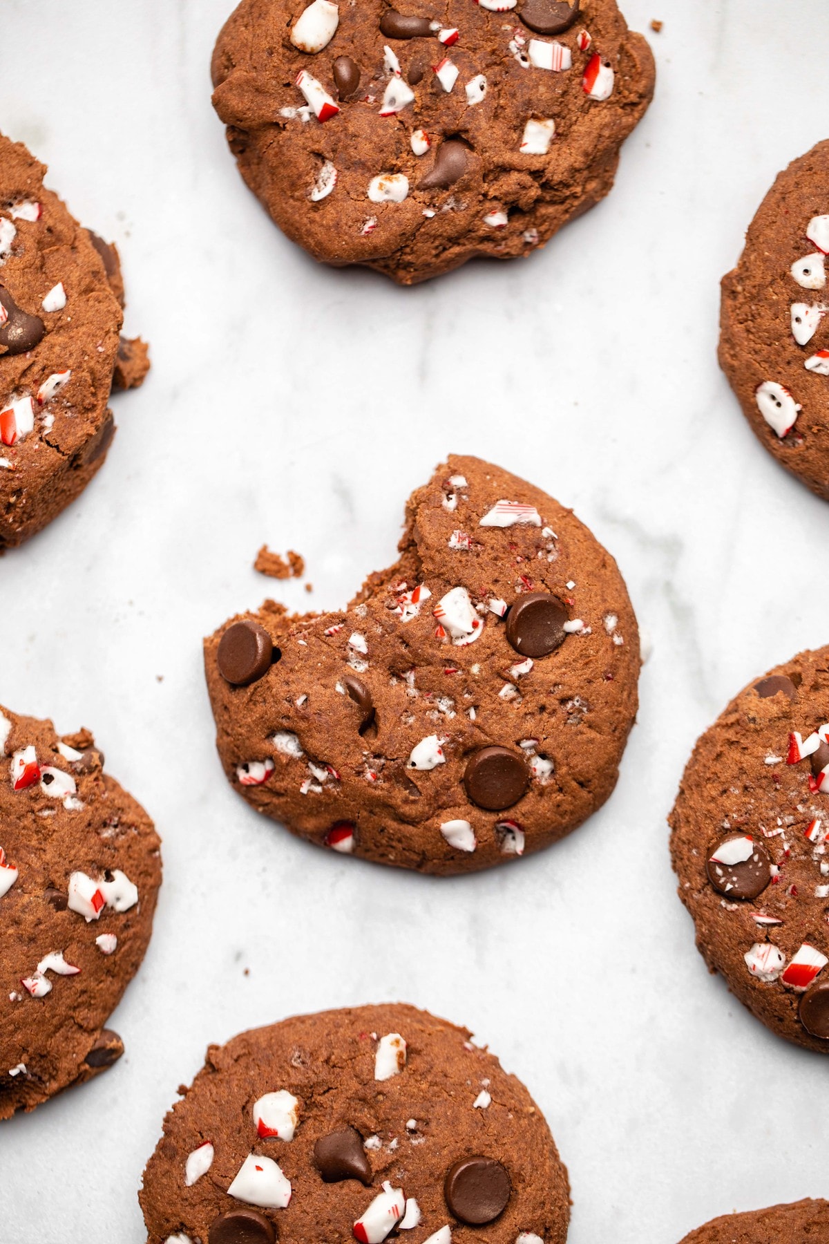 double chocolate peppermint cookies on white marble background with bite taken out of one cookie