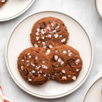three cookies on a white plate next to candy canes and a glass of milk on white marble background