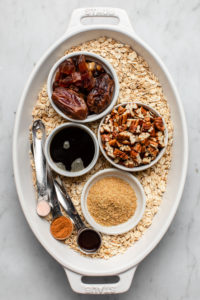 ingredients for maple pecan oatmeal in small white dishes in larger white dish on marble background