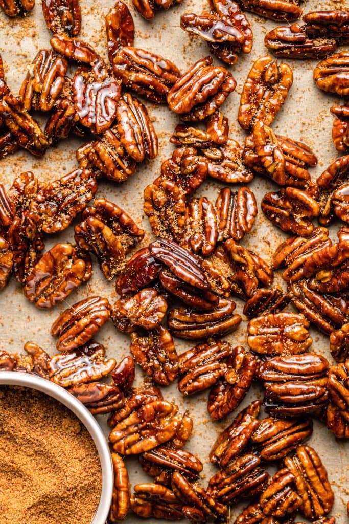 candied pecans on parchment paper with coconut sugar sprinkled on top