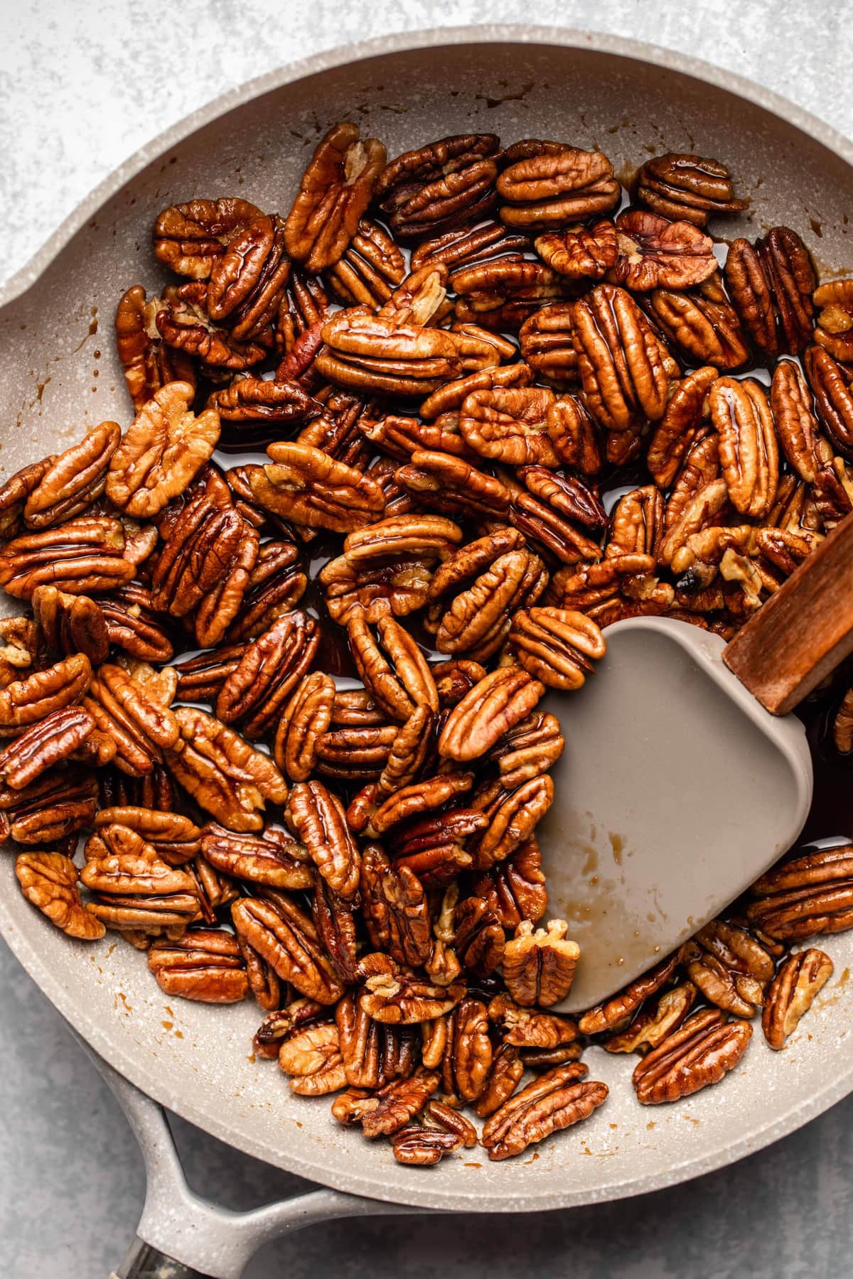 pecans with sugar and water mixture in light tan saucepan with spatula