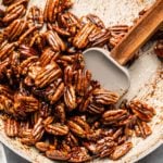 sticky cooked candied pecans in tan saucepan with gray spatula
