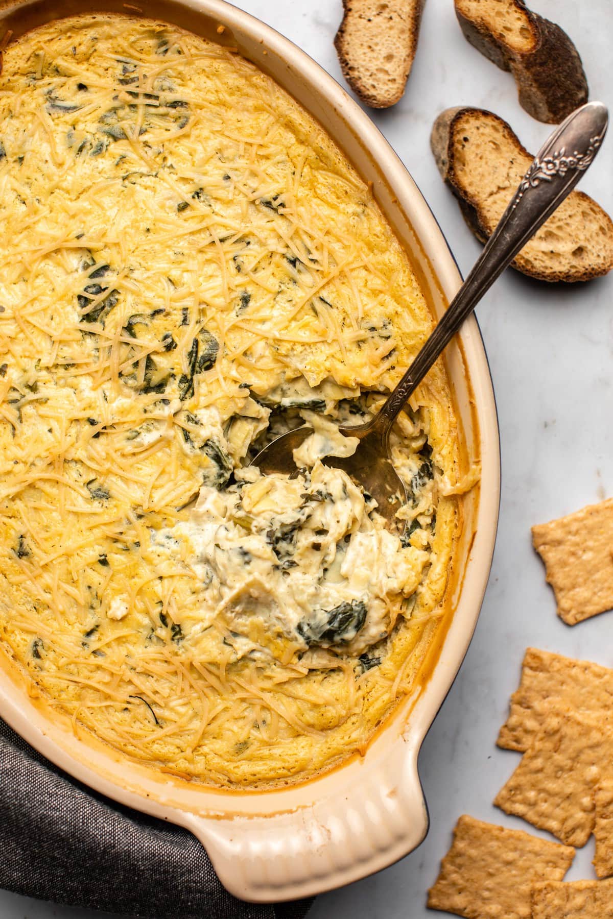 baked spinach and artichoke dip with spoon in dip and crostini and crackers on side