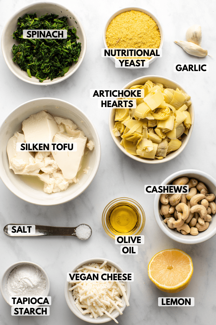 ingredients for vegan spinach and artichoke dip in small bowls on marble background