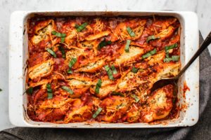 vegan stuffed shells with red sauce and basil in white baking dish on marble background