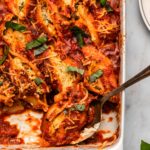 vegan stuffed shells topped with fresh basil in white casserole dish with metal serving spoon