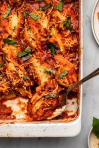 vegan stuffed shells topped with fresh basil in white casserole dish with metal serving spoon