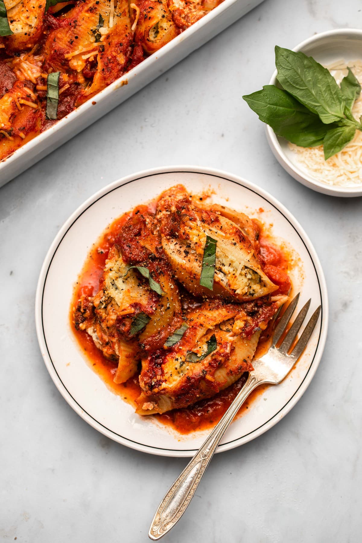 vegan stuffed shells with red sauce and fresh basil on small white plate on marble background