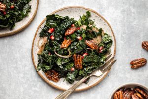 winter kale salad on small speckled white plate on textured blue background