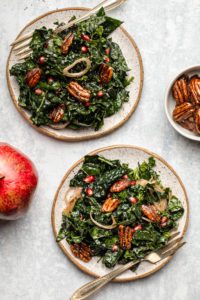 two small white plates of kale salad with forks on blue textured background