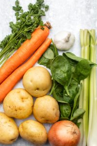 vegetable ingredients for potato spinach soup on marble background