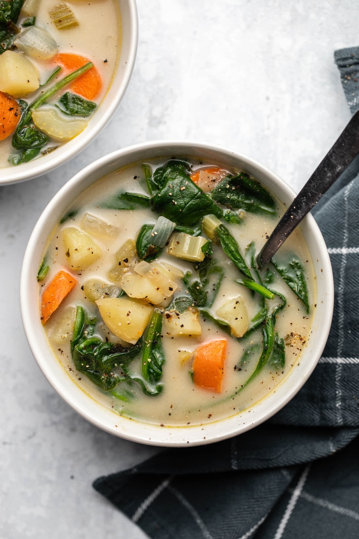 potato spinach soup in white bowl with spoon on marble background