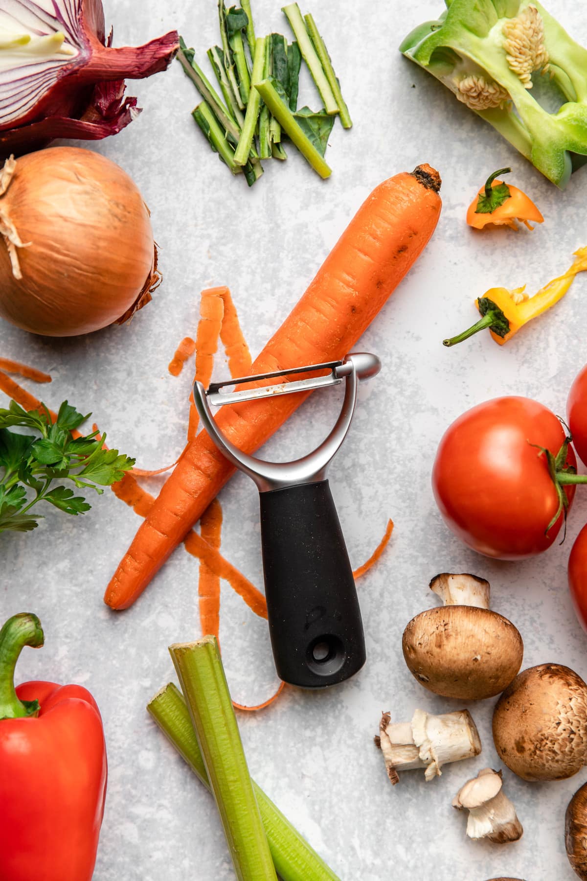 vegetables to include in vegetable broth with vegetable peeler on marble background