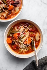 two white bowls of minestrone soup topped with vegan parmesan cheese on marble background