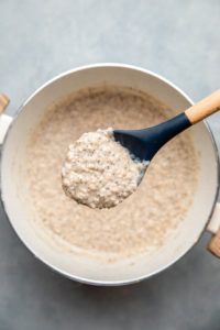 spoon of cooked lemon poppyseed oatmeal over large white pot