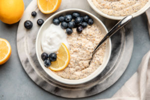 lemon poppyseed oatmeal in white bowl on marble background surrounded by lemons and blueberries
