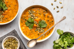 white bowl of smoky sweet potato soup topped with pumpkin seeds and cilantro on marble background