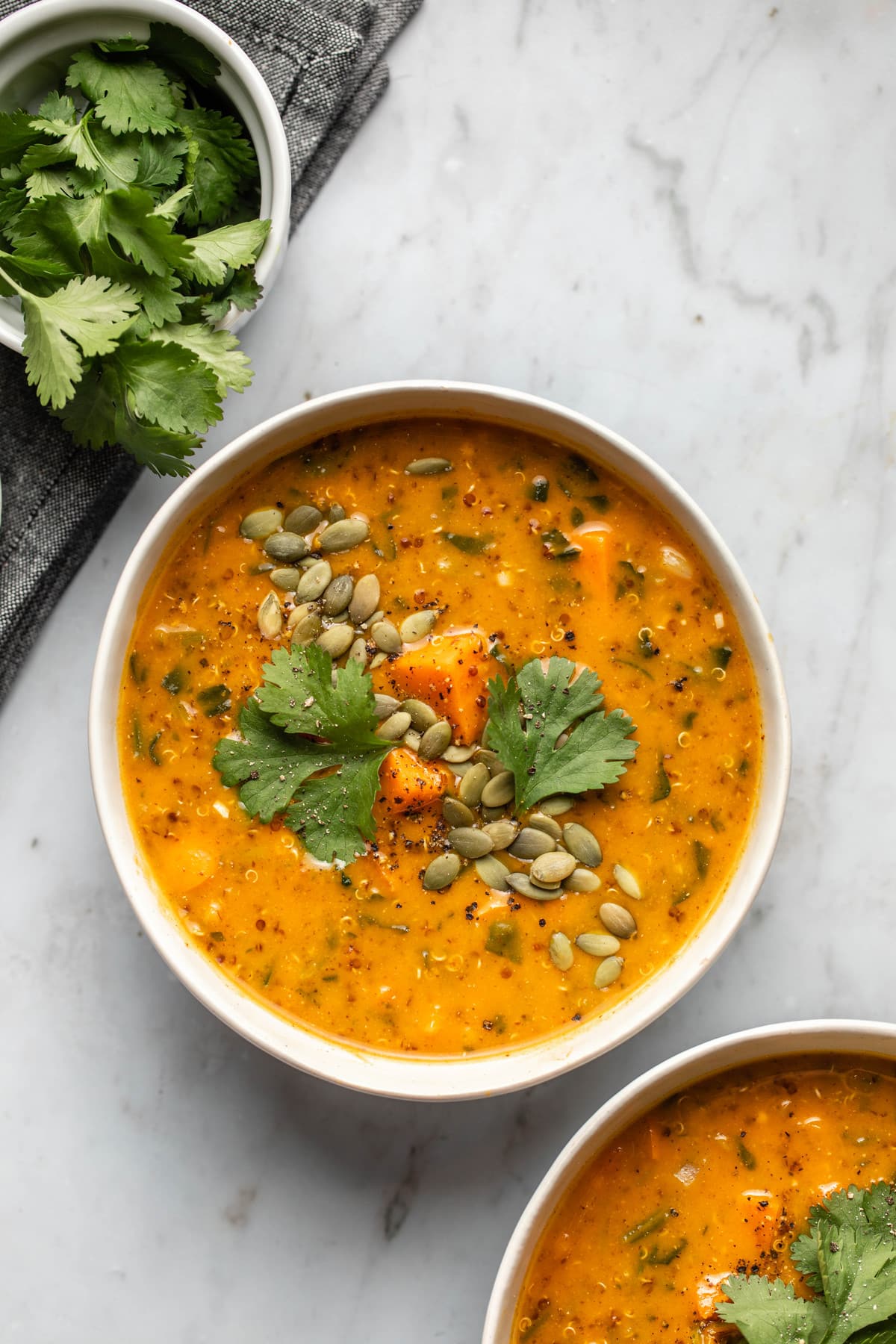 two bowls of smoky sweet potato soup topped with pepitas and cilantro on marble background